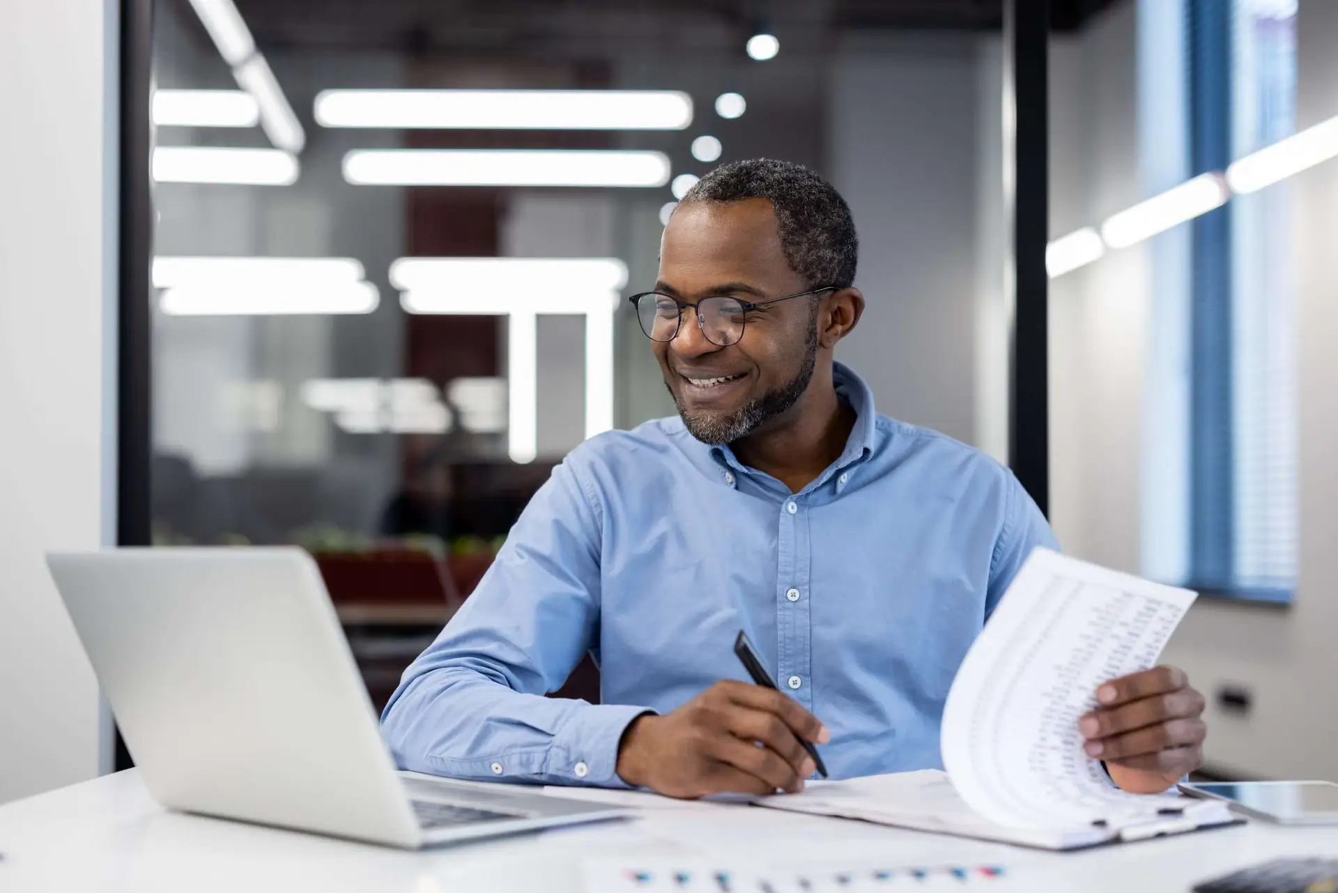 Mature businessman working at desk in modern office analyzing reports and using laptop with focus and confidence Professional man smiling as he reviews financial documents